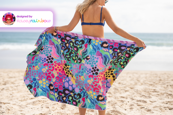 Multicolored recycled sand-free beach towel with leopard and geometric patterns, held open on beach.