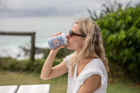 Woman drinking from a Sound of Summer Cooler & Coffee Cup by the ocean