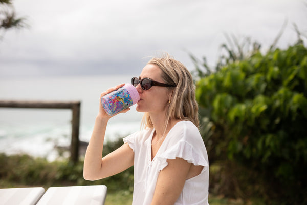 Woman drinking from a Kasey Rainbow Cooler & Coffee Cup by the ocean
