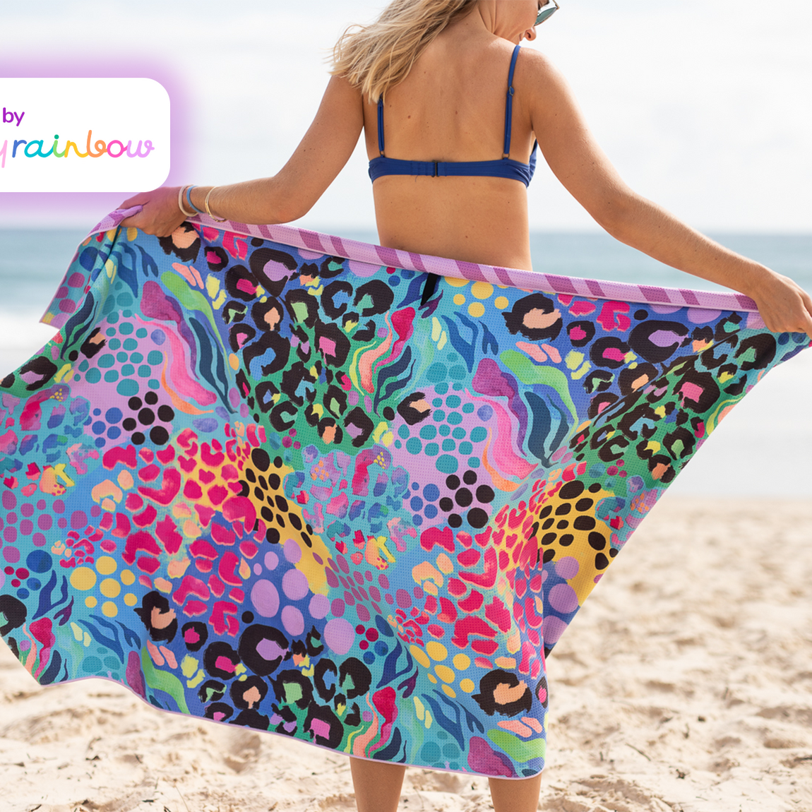 Multicolored recycled sand-free beach towel with leopard and geometric patterns, held open on beach.