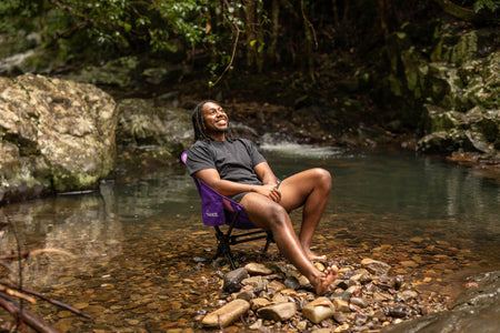 Man laughing in the Mulberry Purple camping chair at a rainforest creek