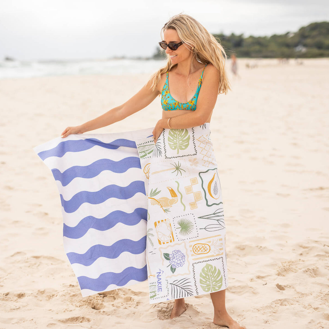 Beach towel with blue wavy stripes and white botanical print design, displayed on sand at beach