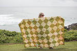Retro Shores sustainable down puffy blanket in olive, cream, and peach diamond pattern, displayed outdoors by ocean. preview #8