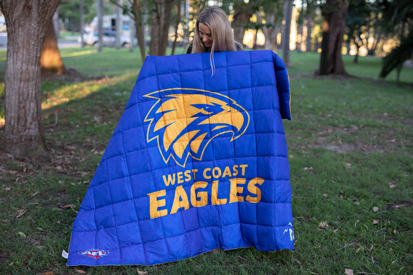 Blue quilted puffy blanket with West Coast Eagles logo and gold text on front, displayed outdoors.