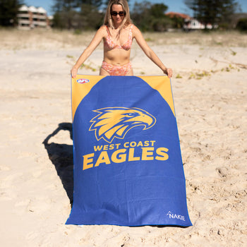 Blue West Coast Eagles beach towel with yellow eagle logo, held by person on sand at beach