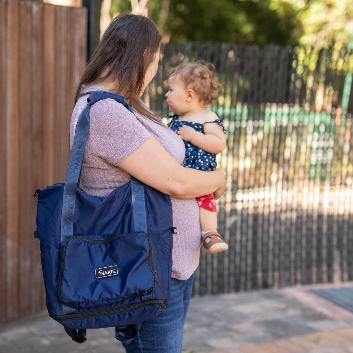Navy recycled tote bag with shoulder straps and front pocket, worn by woman holding toddler outdoors
