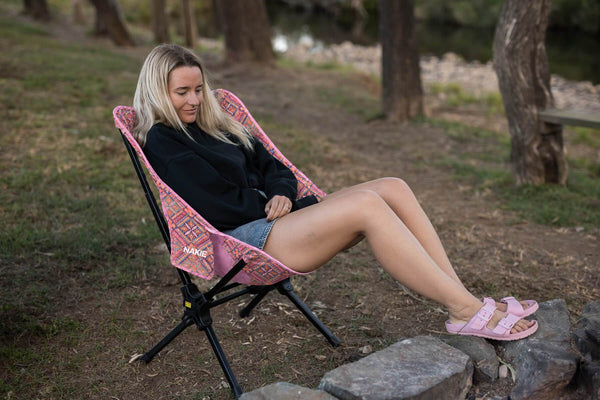 Woman relaxing in the Rosy Tides Camping Chair by the campfire