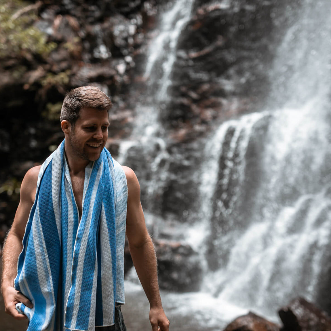 Blue and white striped recycled beach towel draped around man's shoulders near waterfall
